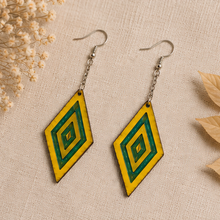 Cargar imagen en el visor de la galería, Aurora Step wooden earrings arranged on neutral linen, showing the vivid yellow wood, green resin geometric accents, silver-tone chains and hooks.