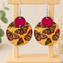 Cargar imagen en el visor de la galería, Hand-painted butterfly wooden earrings on a light wood stand with silver-tone hypoallergenic hooks.