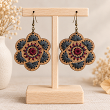 Cargar imagen en el visor de la galería, Crimson Roots embroidered wooden earrings displayed front-facing on a light wood stand against a warm cream background.