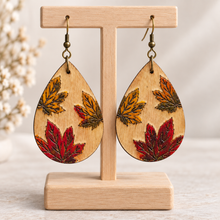 Cargar imagen en el visor de la galería, Leaf Whispers engraved wooden earrings with hand-painted autumn leaves on a light wood stand