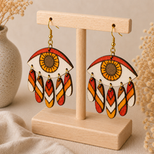Cargar imagen en el visor de la galería, Radiant Eye hand-painted wooden earrings shown at an angle on the standard light wood stand, highlighting the layered dangling construction.