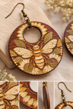 Cargar imagen en el visor de la galería, Close-up of Sunset Honey Bee wooden earring showing natural wood grain, laser-engraved bee and sunflower details, and hand-painted accents