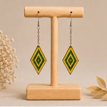 Cargar imagen en el visor de la galería, Aurora Step wooden earrings shown from the front on a light wood stand, with vivid yellow hand-painted wood, green resin accents, silver-tone chains and hooks.
