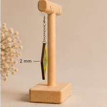 Cargar imagen en el visor de la galería, Side view of Aurora Step wooden earrings on a light wood stand, showing the 2 mm wood thickness, silver-tone chain and hook.
