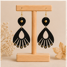 Cargar imagen en el visor de la galería, Ebony Moon wooden earrings shown from the reverse side on a light wood stand, showing the same black-and-gold design on both sides.
