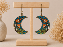 Cargar imagen en el visor de la galería, Hand-painted Enchanted Forest Moon wooden earrings displayed front-facing on a light wood stand.

