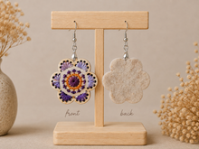Cargar imagen en el visor de la galería, Lavender Bloom hand-embroidered wooden earrings shown front and back on a light wood stand, with the felt-backed reverse visible.
