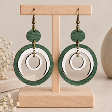 Cargar imagen en el visor de la galería, Lunar Dance articulated green and white wooden earrings on a light wood stand with a clean neutral background
