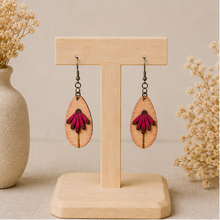 Cargar imagen en el visor de la galería, Mauve Blossom wooden earrings displayed front-facing on a light wood stand, showing the layered deep mauve petals and engraved stem.
