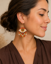 Cargar imagen en el visor de la galería, Radiant Eye hand-painted wooden earring shown at realistic scale on a model wearing a warm cocoa blouse.
