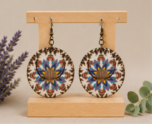 Cargar imagen en el visor de la galería, Reversible mandala wooden earrings on a light wood stand showing the blue and purple mandala side.
