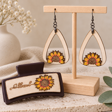 Cargar imagen en el visor de la galería, Sunflower Blessed matching set with lightweight wooden earrings on a light wood stand and a 3.5-inch dark brown hair clip with layered hand-painted sunflower detail.

