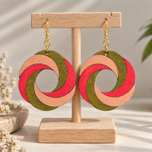 Cargar imagen en el visor de la galería, SunTwist Joy hand-painted wooden swirl earrings in coral, peach and olive on a light wood stand with gold-tone hooks
